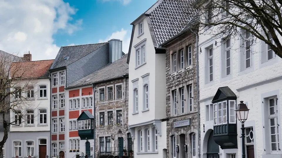 Charmante historische Häuser säumen eine alte Straße in Aachen, Deutschland, unter einem strahlend blauen Himmel.